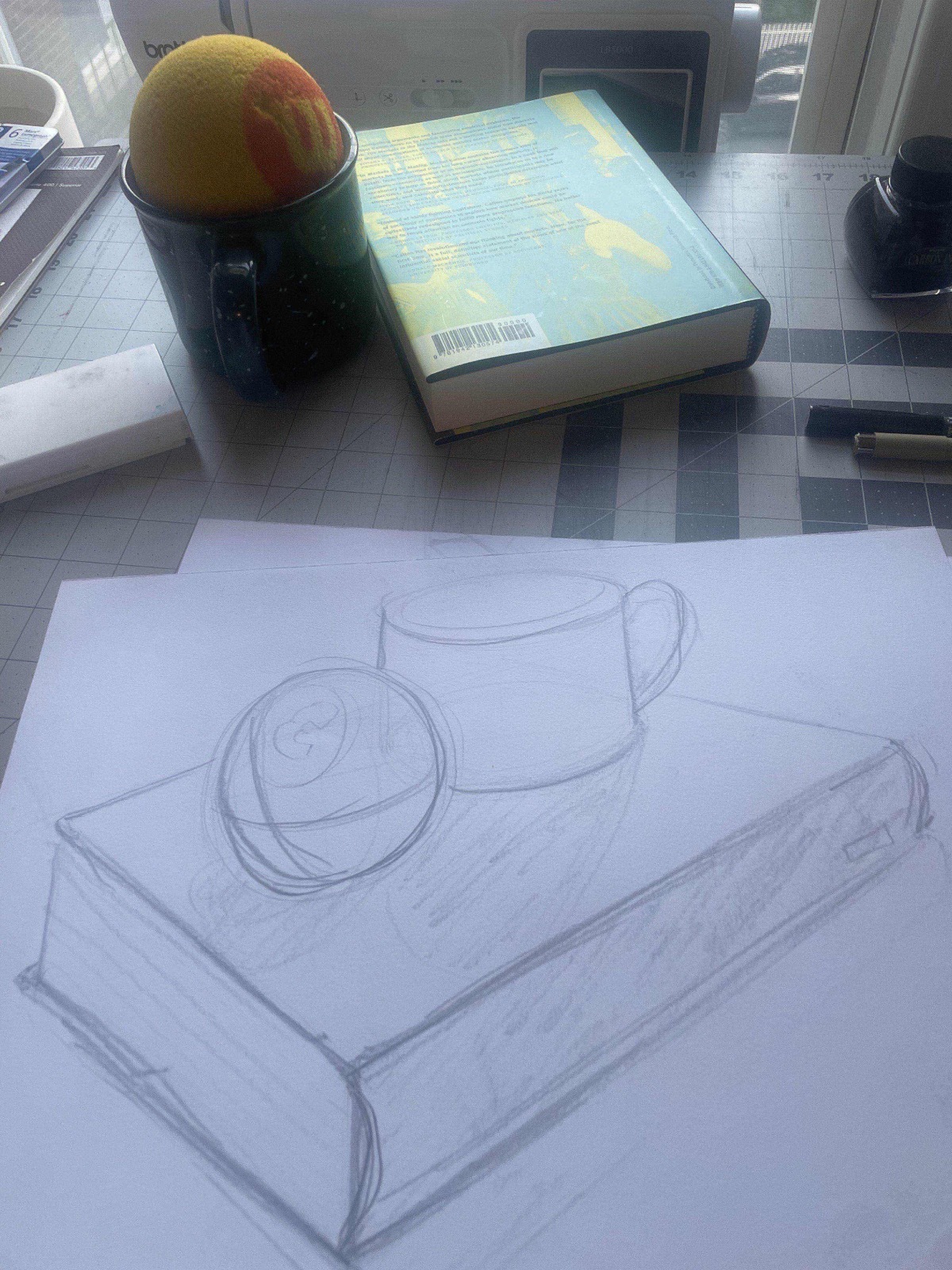 still life of a mug and ball on a book, with pencil drawing of the volumetric forms
